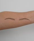 Two small, thin eyebrows drawn on a person's arm against a plain background
