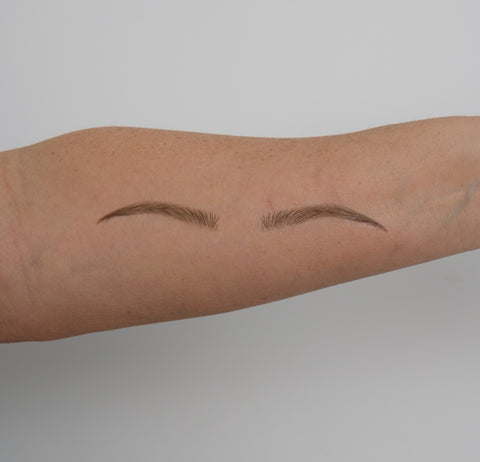 Two small, thin eyebrows drawn on a person's arm against a plain background