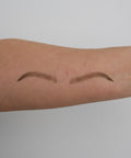 Two arched eyebrow tattoos on a person's arm against a plain background