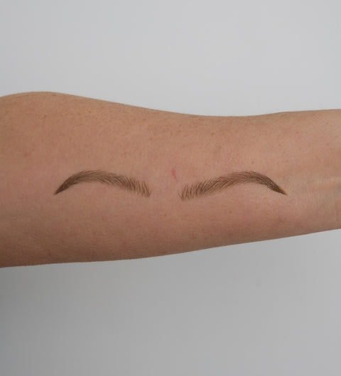 Two arched eyebrow tattoos on a person's arm against a plain background
