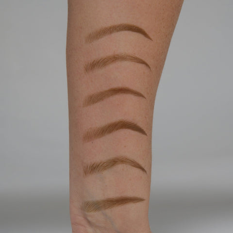 Set of eyebrow pencils on a person's arm against a neutral background