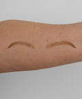 Two arched eyebrow tattoos on a person's arm against a plain background