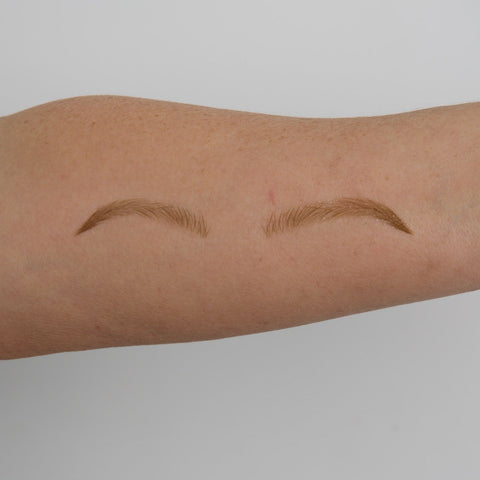 Two arched eyebrow tattoos on a person's arm against a plain background