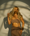 Woman in a brown outfit standing against a textured wall with shadow patterns