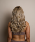 Person with long, wavy blonde hair wearing a patterned top against a neutral background