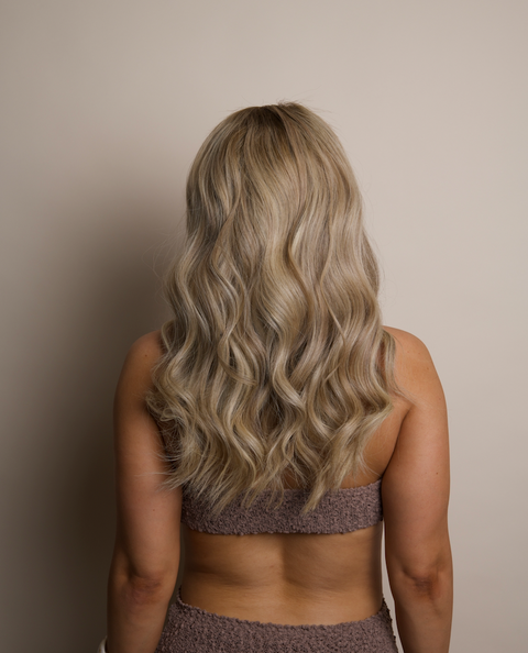 Person with long, wavy blonde hair wearing a patterned top against a neutral background
