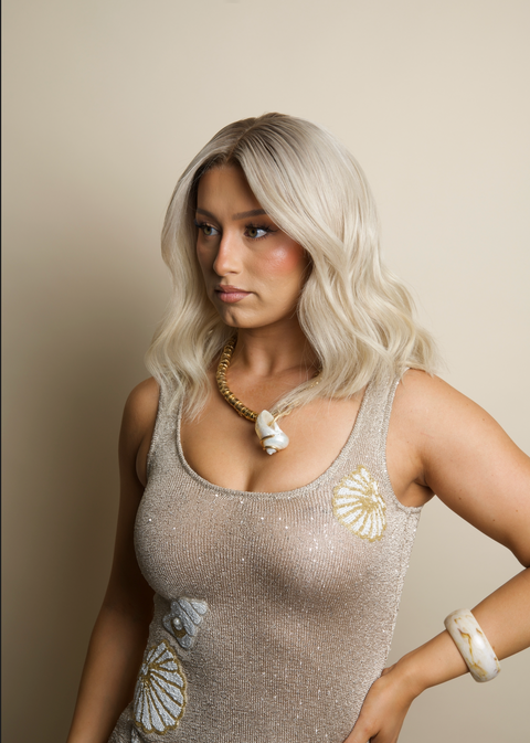 Woman wearing a sparkly top with shell designs against a beige background