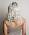 Person with wavy silver hair wearing a sparkly silver top against a neutral background