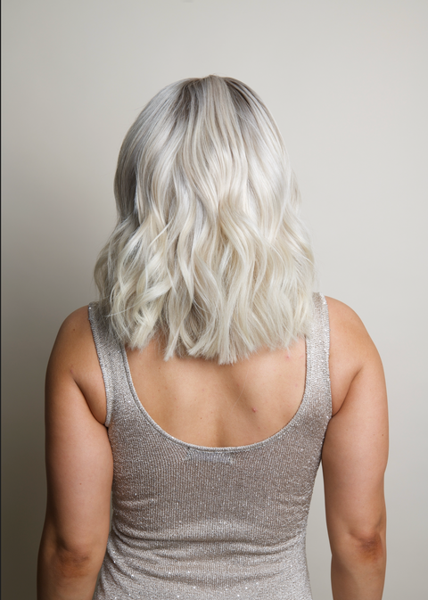 Person with wavy silver hair wearing a sparkly silver top against a neutral background