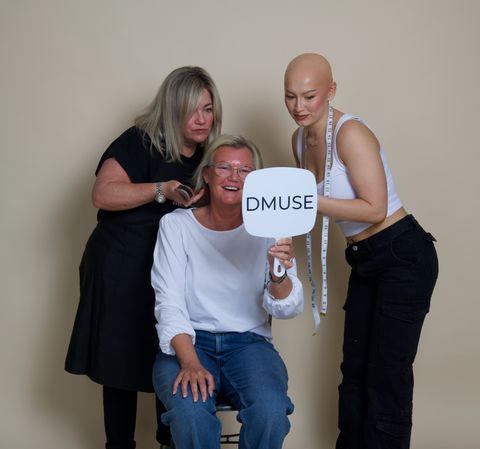 Three women with a mirror displaying 'DMUSE' in a studio setting.