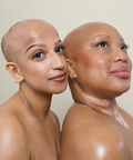 Two women with bald heads standing close to each other against a plain background