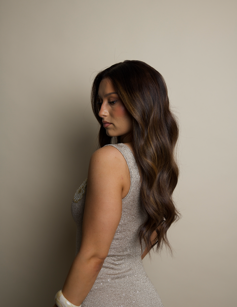 Woman with long, wavy hair wearing a silver dress against a beige background