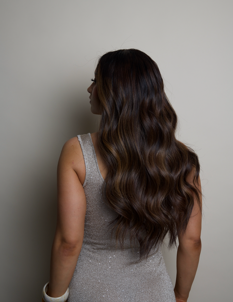 Woman with long, wavy hair wearing a silver dress against a neutral background
